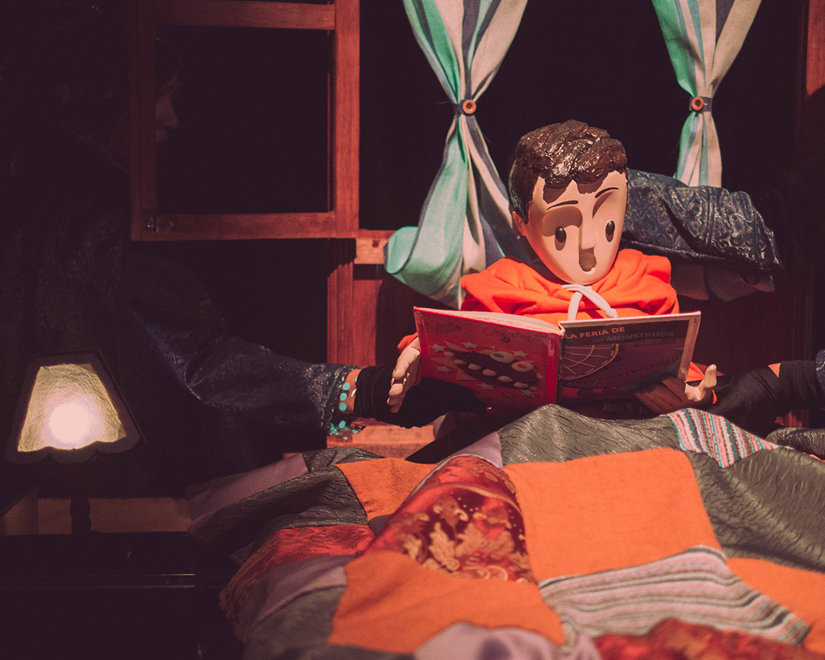 Títere de Colectivo Pies Hinchados leyendo un libro de cuentos sobre un escenario teatral